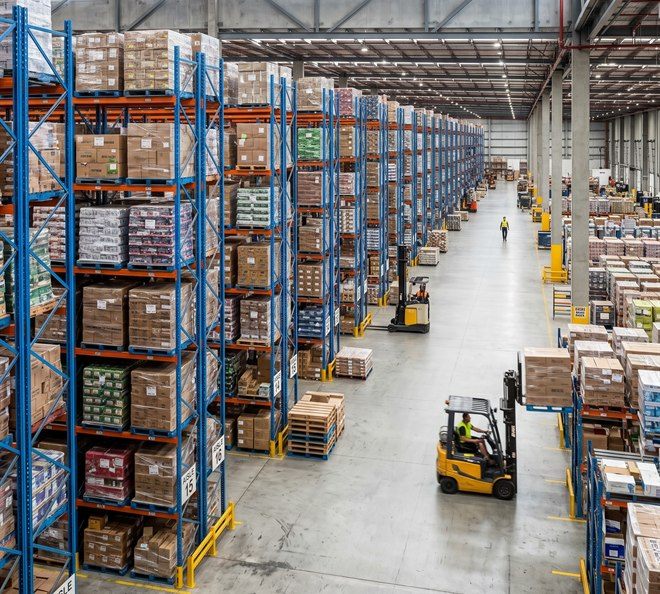 Galpão logístico com fileiras de porta-paletes de vários níveis e empilhadeiras em operação